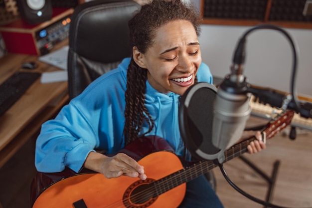 Foto jong getalenteerd meisje dat gitaar speelt en een lied zingt in een microfoon die repeteert in een professionele opnamestudio