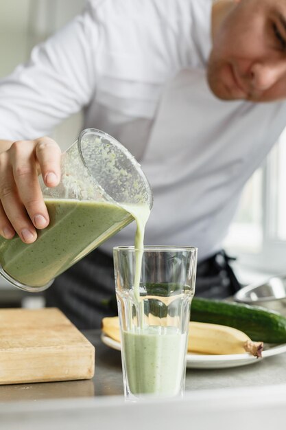 Jong gewas mannetje in uniform gieten verse smoothie van groene kleur in schoon glas