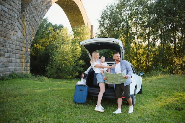 Jong gezin drie mensen in witte kleren hebben picknick. Mooie ouders en dochter reizen met de auto tijdens de zomervakantie. Scène in park