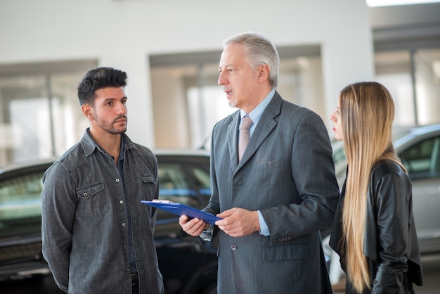 Jong gezin in gesprek met de verkoper en het kiezen van hun nieuwe auto in een showroom