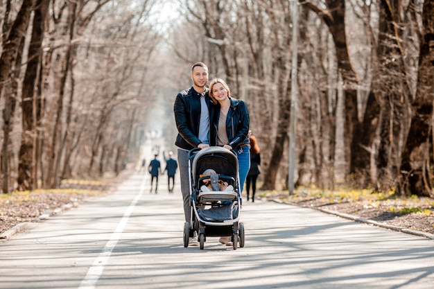 Jong gezin lopen in het park in het voorjaar met een peuter in een wandelwagen. Gelukkige ouders