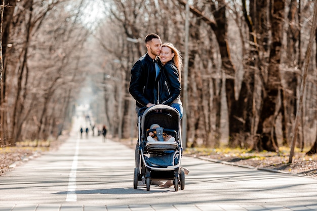 Jong gezin lopen in het park in het voorjaar met een peuter in een wandelwagen. Gelukkige ouders