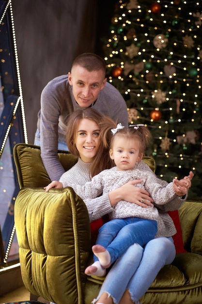 Jong gezin met kleine babymeisje in gezellig interieur met feestelijke kerstboom is poseren Goed humeur en plezier samen Merry Christmas concept Gelukkig ouderschap concept