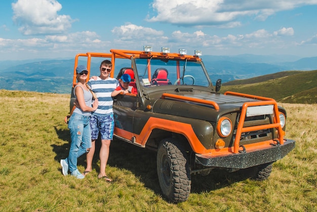 Jong gezin poseren in de buurt van suv auto met prachtig uitzicht op bergen reizen concept