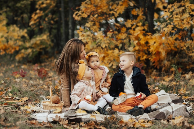Jong gezin zittend op een picknickkleed, omarmen en genieten van een mooie herfstpicknick in de natuur.