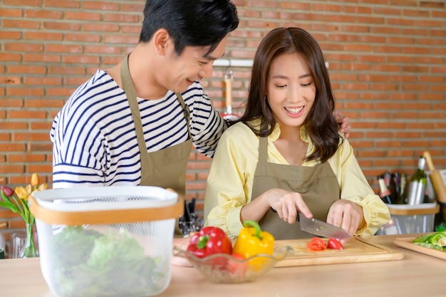 Jong glimlachend Aziatisch paar dat een schort in het kookconcept van de keukenruimte draagt