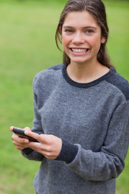 Jong glimlachend meisje dat de camera bekijkt terwijl het gebruiken van haar cellphone