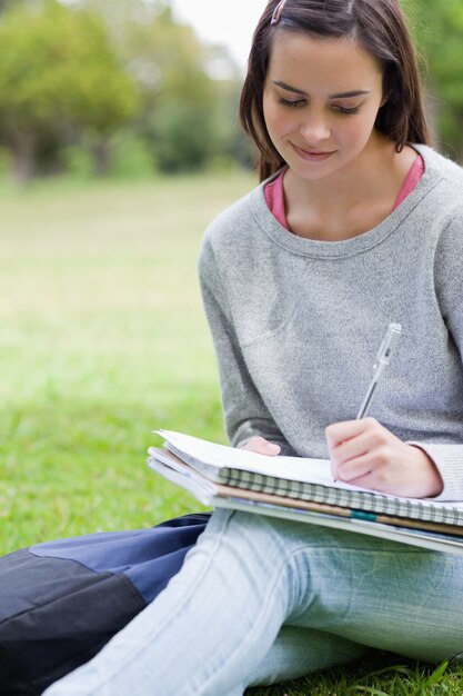 Jong glimlachend meisje die op haar notitieboekje schrijven terwijl het zitten in een park