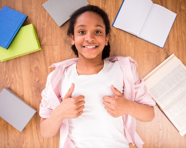 Jong glimlachend mulatschoolmeisje dat op de vloer legt.