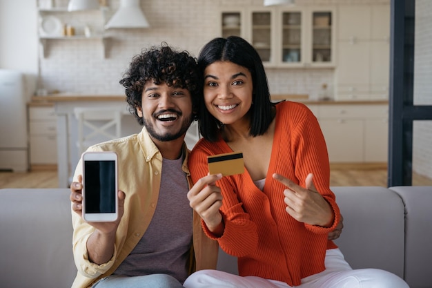 Jong glimlachend multiraciaal stel met creditcard met mobiele app om thuis online te winkelen