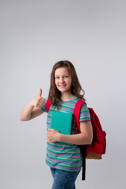 Jong glimlachend schoolkind met rugzak op haar schouders en notitieboekje