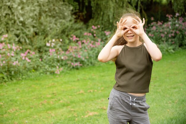 Jong glimlachend tienermeisje die teken met handen, op groene, openluchtparkachtergrond tonen