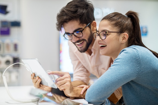 Jong hipster modieus glimlachend multiraciaal paar die het nieuwe model van een tablet met een potlood in de technologie-opslag testen.