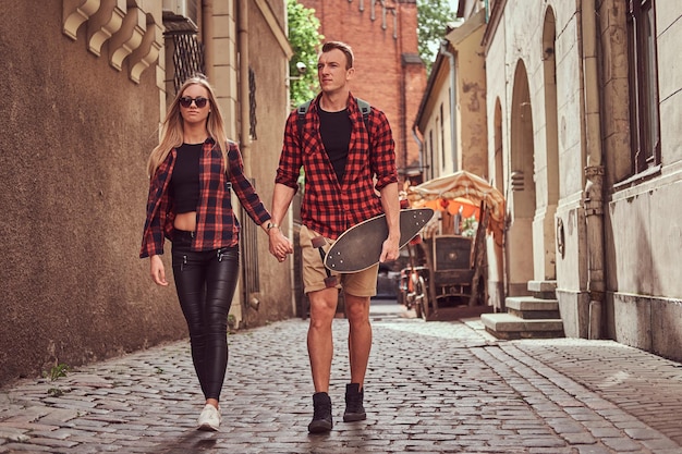 Jong hipsterpaar, knappe schaatser en zijn vriendin die door de oude smalle straatjes van Europa lopen.