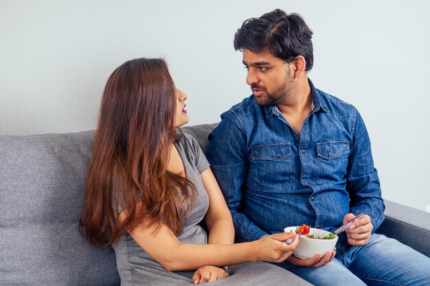 Jong Indiaas stel zit in hun woonkamer en eet groentesalade