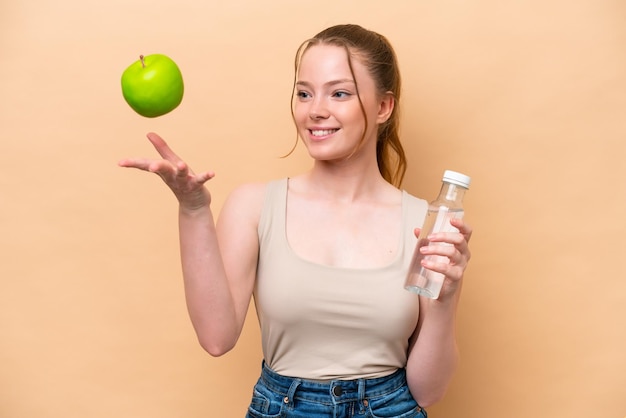 Jong Kaukasisch meisje geïsoleerd op beige achtergrond met een appel en met een fles water