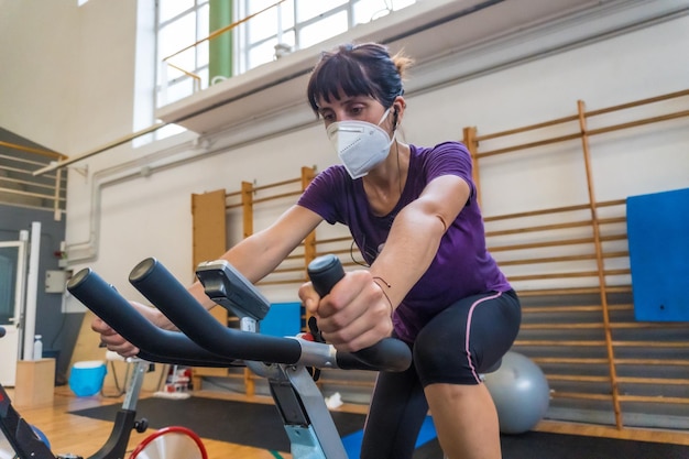 Jong kaukasisch meisje met een gezichtsmasker op een hometrainer