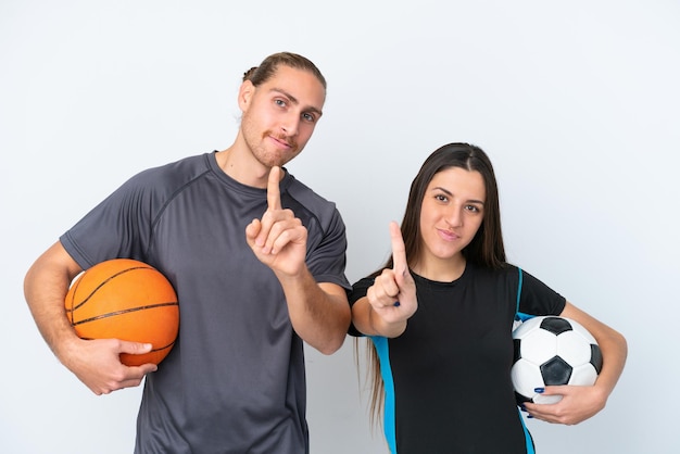 Jong Kaukasisch paar dat basketbal en voetbal speelt dat op witte achtergrond wordt geïsoleerd en een vinger toont en opheft