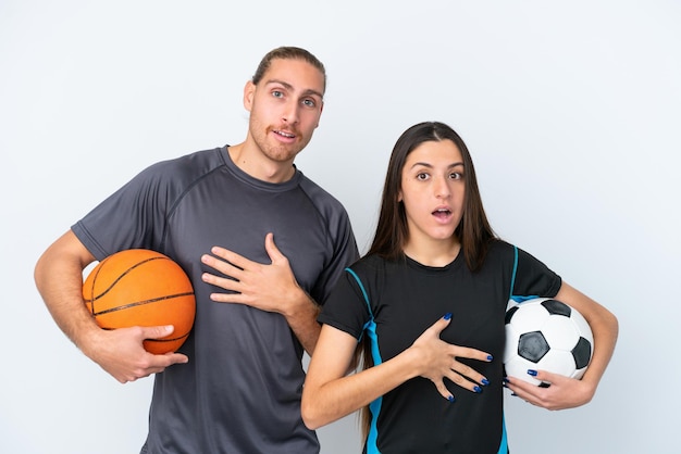 Jong Kaukasisch paar dat basketbal en voetbal speelt geïsoleerd op een witte achtergrond met verrassing en geschokte gezichtsuitdrukking