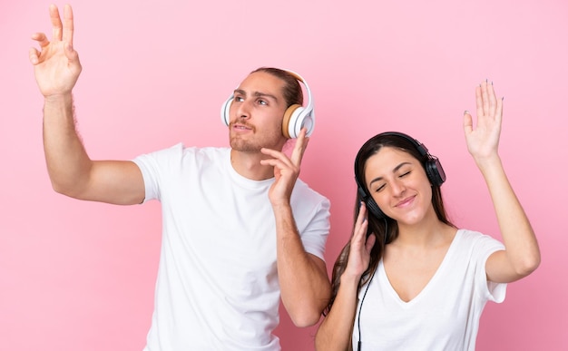 Jong Kaukasisch paar geïsoleerd op roze achtergrond muziek luisteren en dansen