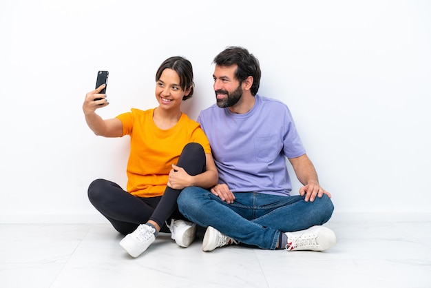 Jong Kaukasisch paar zittend op de vloer geïsoleerd op een witte achtergrond maken een selfie met de mobiel