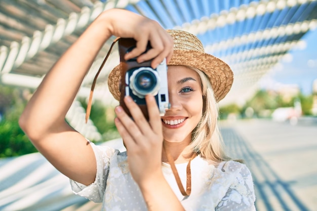 Jong kaukasisch toeristenmeisje dat gelukkig lacht met behulp van vintage camera op straat van de stad