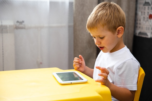 Jong kind jongen spelen of cartoon kijken op de tablet binnen.