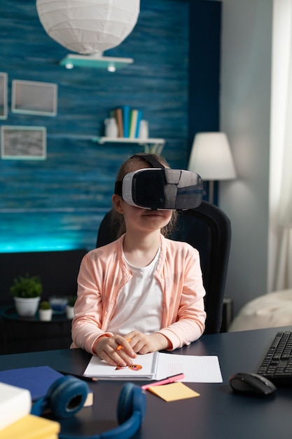 Jong kind leren les cursus met vr bril technologie gadget aan huis bureau. slimme schoolmeisjesleerling die vision-apparatuur gebruikt voor de studiemethode voor amusement op de basisschool