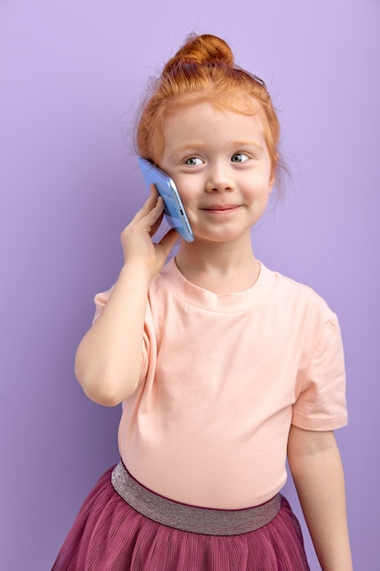 Jong kind meisje communiceert op de mobiele telefoon glimlacht en praat geïsoleerd op paars