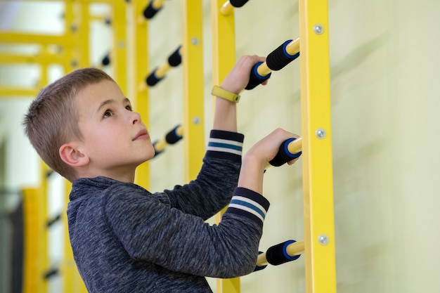 Jong kindjongen die op een bar van de muurladder uitoefenen binnen de ruimte van de sportengymnastiek in een school.