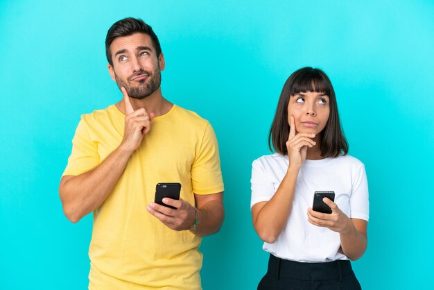 Jong koppel geïsoleerd op blauwe achtergrond met behulp van mobiele telefoon en denken