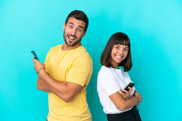 Jong koppel geïsoleerd op blauwe achtergrond met een mobiele telefoon en met gekruiste armen