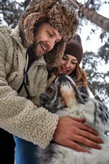 Jong koppel glimlachend en plezier in het winterpark met hun husky hond