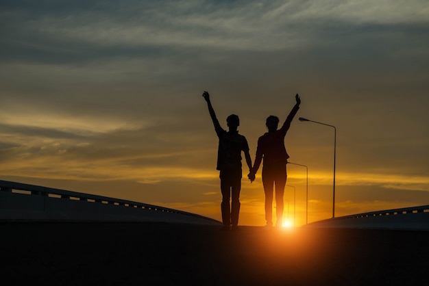 Jong koppel hand omhoog bij zonsondergang op de weg.