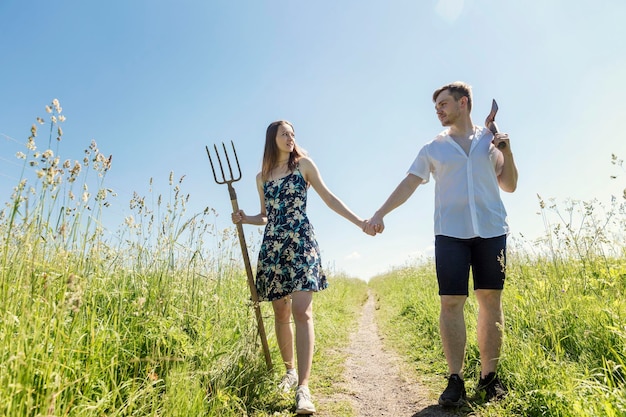 Jong koppel in een veld in een dorp op een zonnige zomerdag Een man met een bijl een meisje met een hooivork loopt Grote openluchtrecreatie