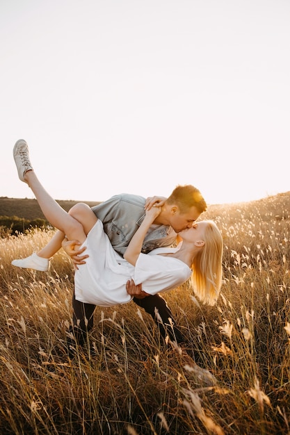 Jong koppel in een veld met plezier. man met vrouw in zijn armen, kuste haar.