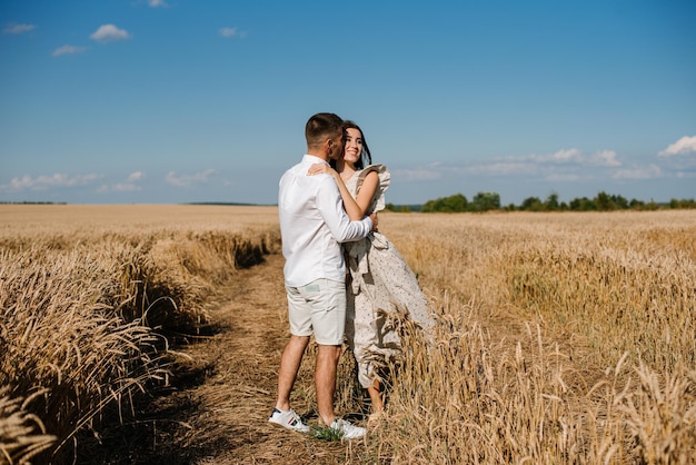 Jong koppel in het tarweveld op zonnige zomerdag. Verliefde paar veel plezier in gouden veld. Romantisch paar in casual kleding outdoodrs op grenzeloos veld