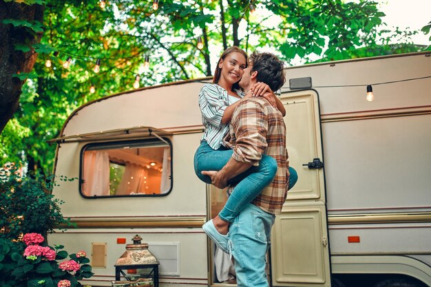 Jong koppel in liefde tijd samen doorbrengen in de buurt van aanhangwagen Knappe bebaarde man en mooie vrouw genieten van gezelschap van elkaar en knuffelen Samen reizen met camper