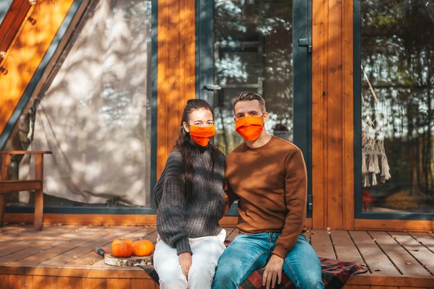 Jong koppel in maskers zittend op het terras van hun huis in de herfst