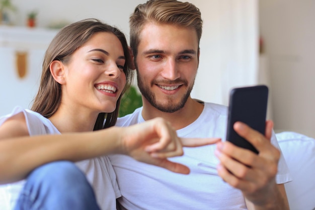 Jong koppel kijken naar online inhoud in een smartphone zittend op een bank thuis in de woonkamer