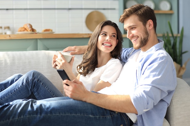 Jong koppel kijken naar online inhoud in een smartphone zittend op een bank thuis in de woonkamer.