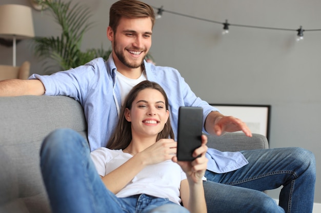 Jong koppel kijken naar online inhoud in een smartphone zittend op een bank thuis in de woonkamer.