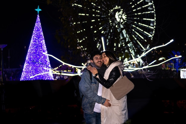 jong koppel knuffelen en genieten van hun bezoek aan een themapark met Kerstmis 's nachts