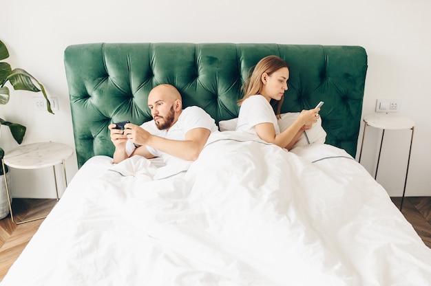 Jong koppel ligt in bed met telefoons