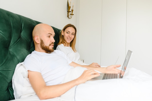 Jong koppel maakt gebruik van laptop in bed. freelancer ochtend.