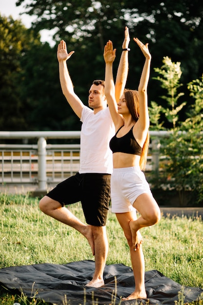 Jong koppel man en vrouw sporten, yoga op stadsgazon, zomeravond, stretching,