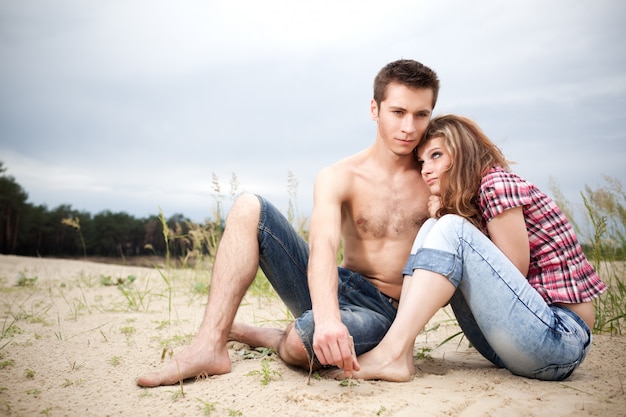 Jong koppel man en vrouw zitten samen op zandgrond op zomerdag