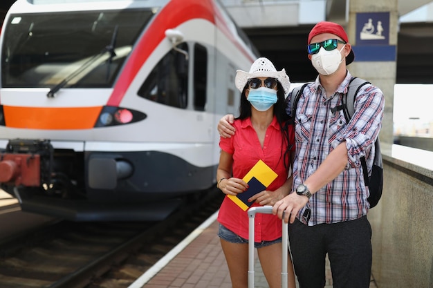 Jong koppel met beschermende medische maskers die in de buurt van de trein staan met kaartjes in hun handen