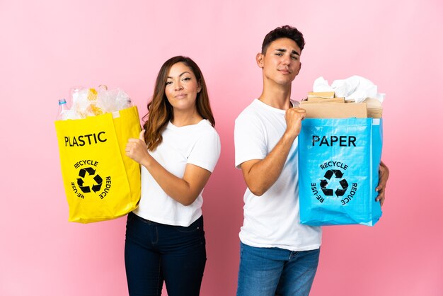 Jong koppel met een tas vol plastic en papier op roze trots en zelfvoldaan