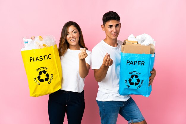 Jong koppel met een zak vol plastic en papier op roze geld gebaar maken